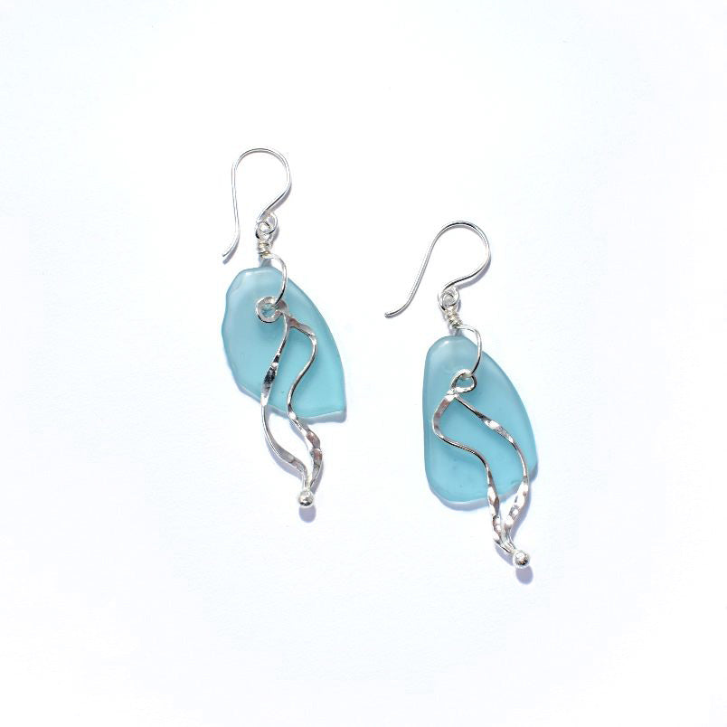 These dangling sea glass earrings have oval shaped glass hangs with sterling silver wires wrapped around it. The wires form swirling designs that depict bull kelp.