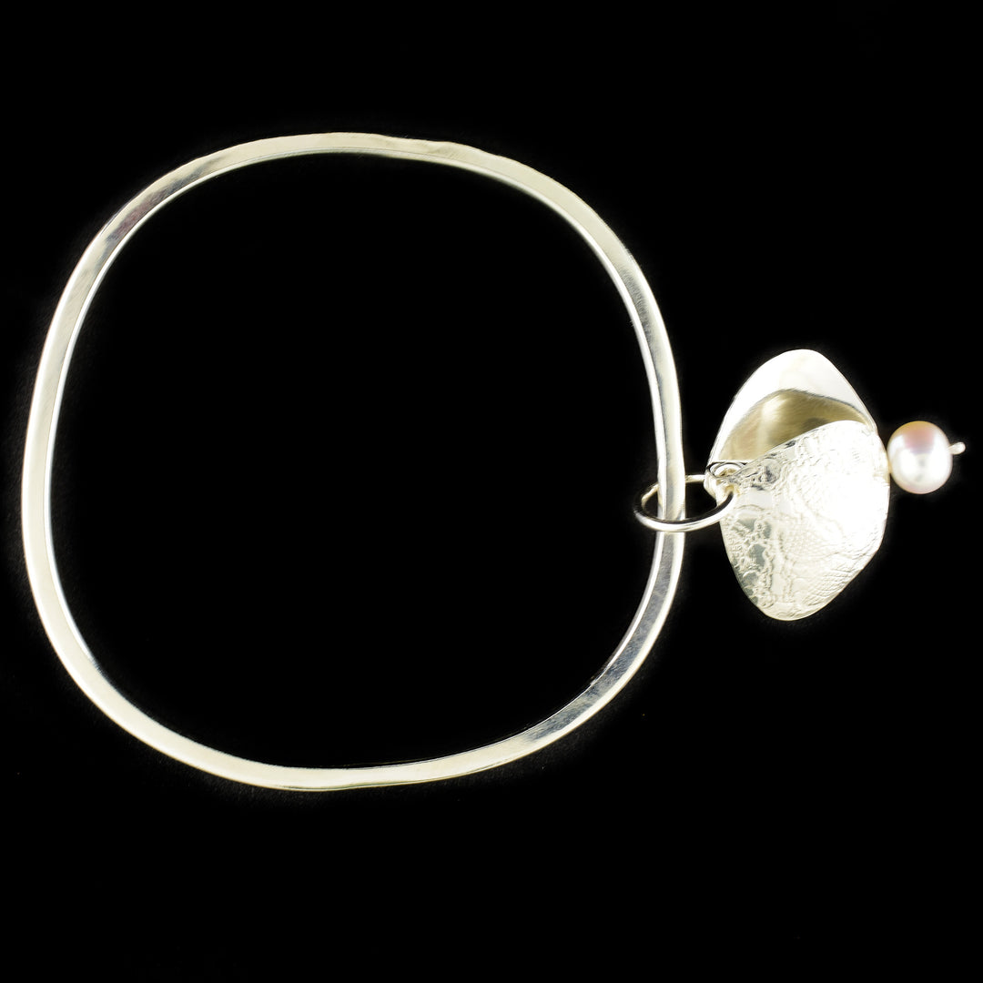 Unique bangle handcrafted by artist Victoria Poynton. Made of sterling silver and a freshwater pearl. Victoria has used vintage French lace to emboss the design on the pendant. Bracelet has a circumference of 8" and pendant measures 1.50" x 0.88" including bail.