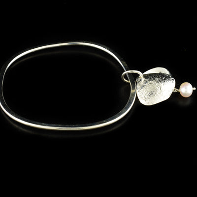 Unique bangle handcrafted by artist Victoria Poynton. Made of sterling silver and a freshwater pearl. Victoria has used vintage French lace to emboss the design on the pendant. Bracelet has a circumference of 8" and pendant measures 1.50" x 0.88" including bail.