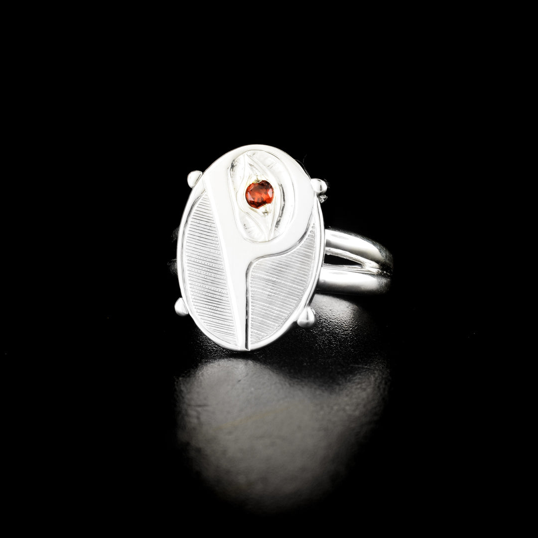 Stunning oval hummingbird ring hand-carved by Haisla artist Hollie Bartlett. Made of sterling silver. Garnet in eye of hummingbird. Oval face of ring measures 0.7" x 0.5". Size 7.