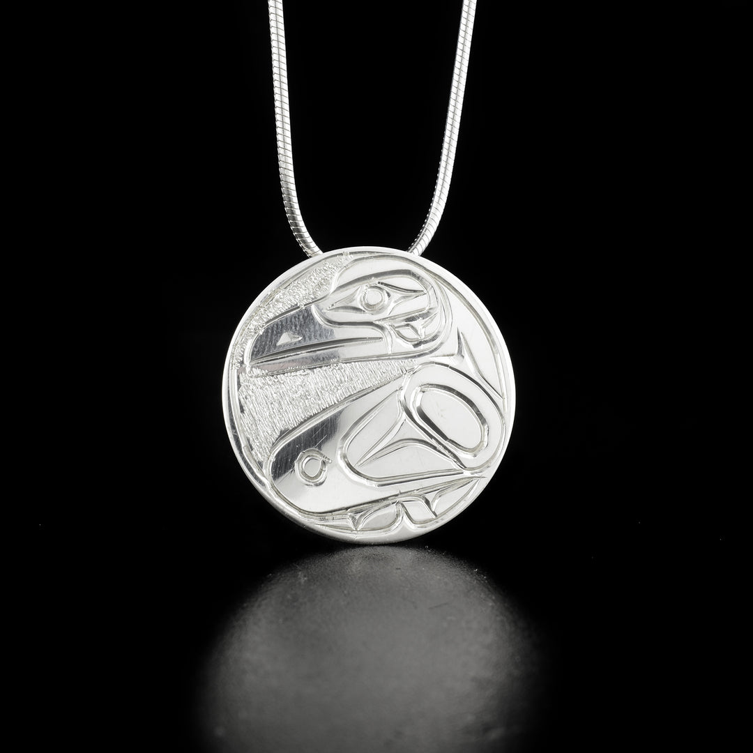 Detailed round raven pendant hand-carved by Kwakwaka'wakw artist Paddy Seaweed. Made of sterling silver. Pendant is 1" in diameter. Hidden bail on back. Chain not included.