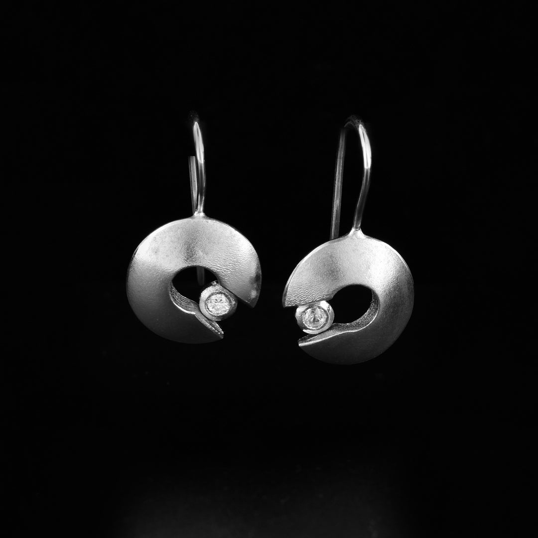 These sterling silver and cubic zirconia earrings have circle hangs with a small circle cutout in the center. There is also a cutout in the side of the hangs where a cubic zirconia gem is held in silver.