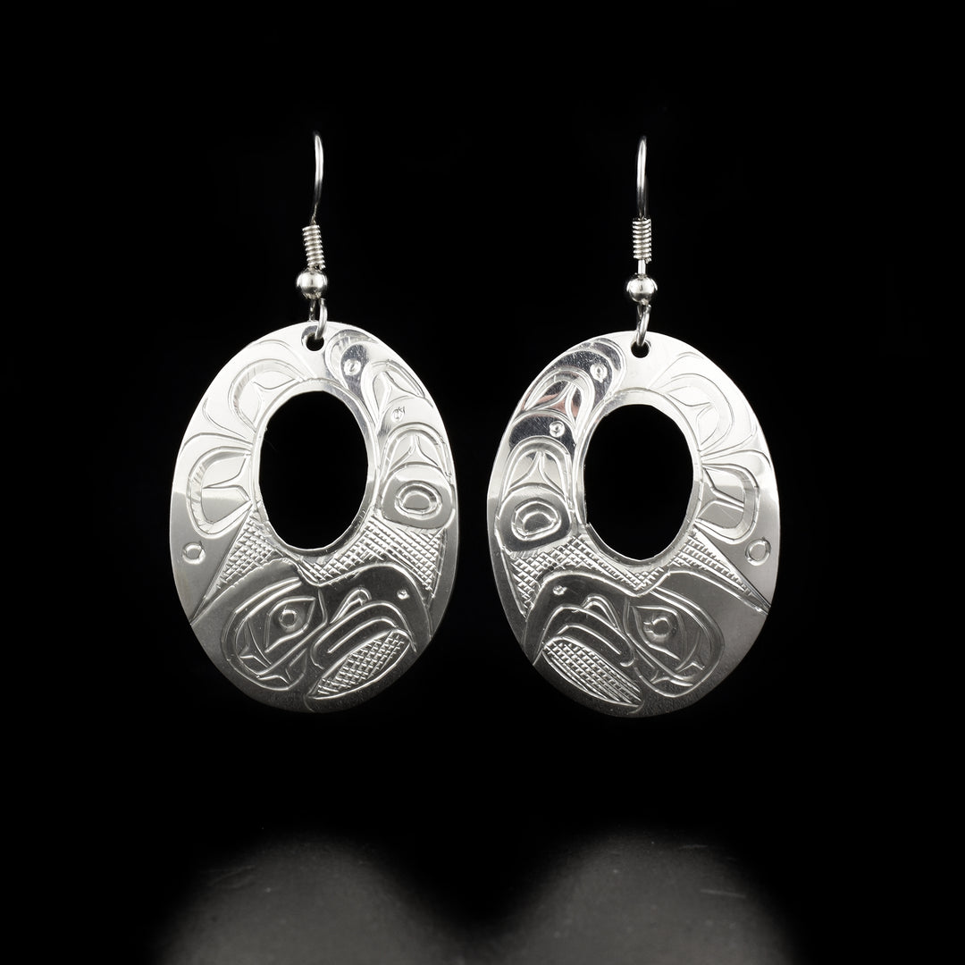 These dangling Eagle earrings are made from sterling silver and have large oval shaped hangs with small cutouts in the center of them. There are beautiful carvings on the surface of the hangs depicting the Eagle and swirling designs.