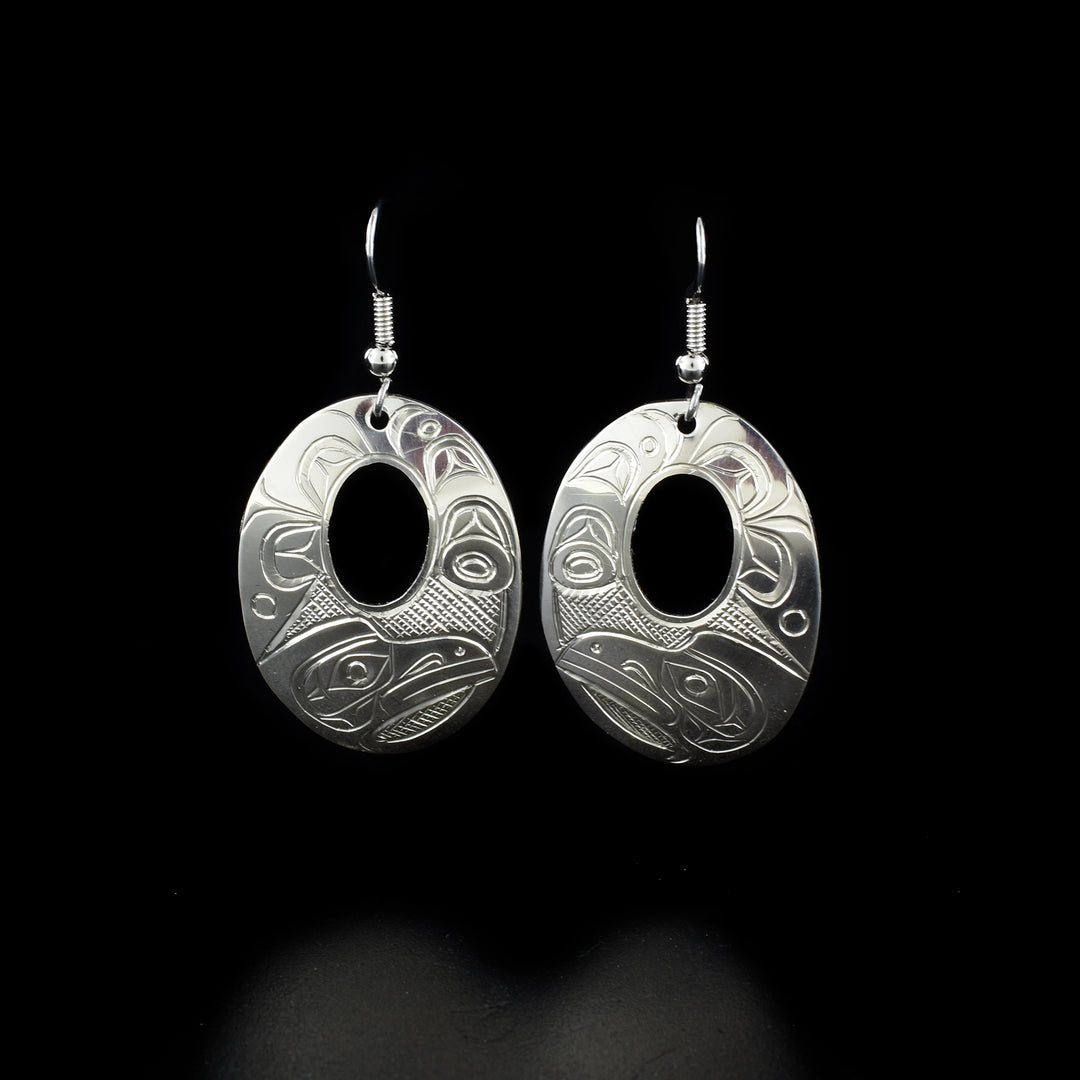These dangling Raven earrings are made from sterling silver and have large oval shaped hangs with small cutouts in the center of them. There are beautiful carvings on the surface of the hangs depicting the Raven and swirling designs.