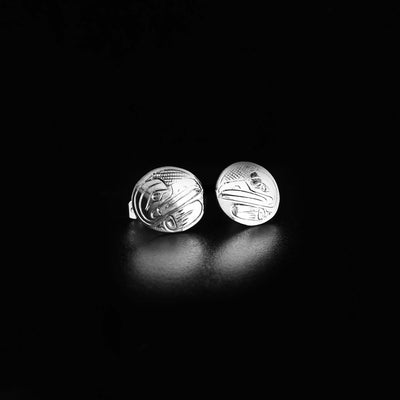 Sterling Silver Raven Stud Earrings by Travis Henry. The design on each earring depicts the profile of a raven's head facing inward. The raven has a thick, long beak and a wing underneath its head. The background has been neatly hand-carved into a crisscross pattern to allow for the raven to stand out.