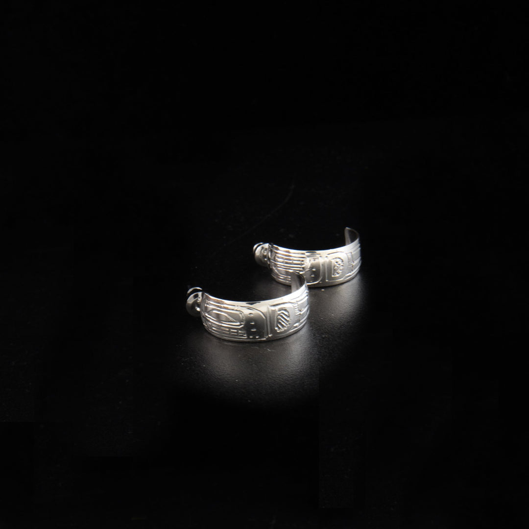 These sterling silver Orca earrings have small, wide hoops with gaps in the back. There are depictions of the Orca carved into the surface of these stud hoop earrings.