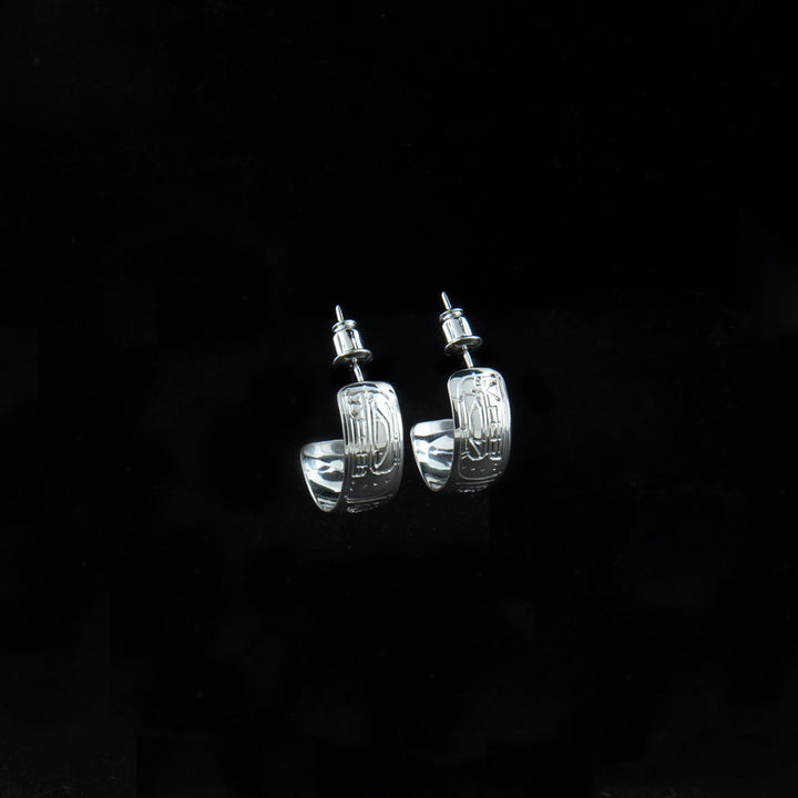 These sterling silver Orca earrings have small, wide hoops with gaps in the back. There are depictions of the Orca carved into the surface of these stud hoop earrings.