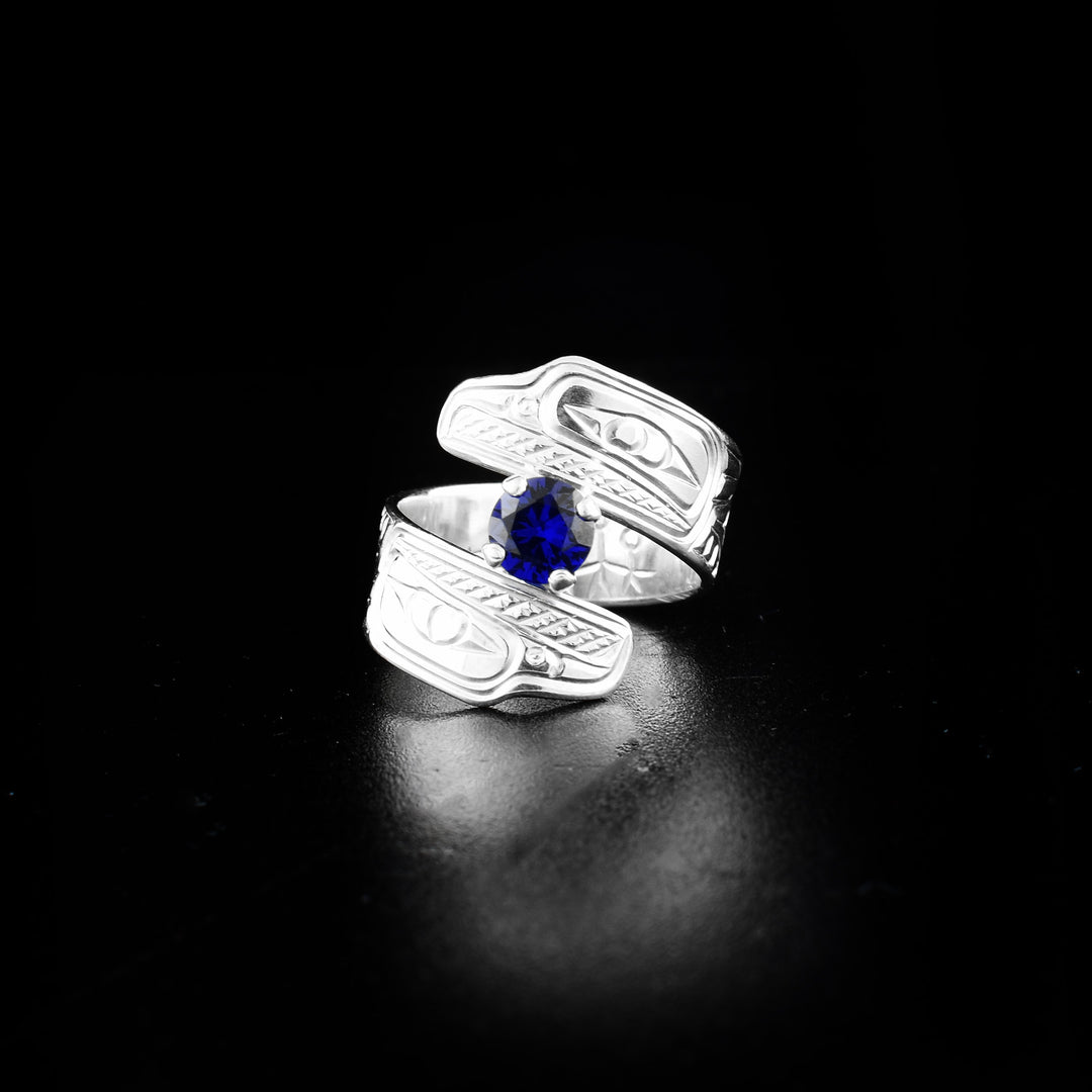 Raven wrap ring hand-carved by Coast Salish and Cree artist Richard Lang. Made of sterling silver and a lab-grown stone. Band is 0.31" wide, with the flexible wrap design giving the ring a comfortable fit. Size 8.5.