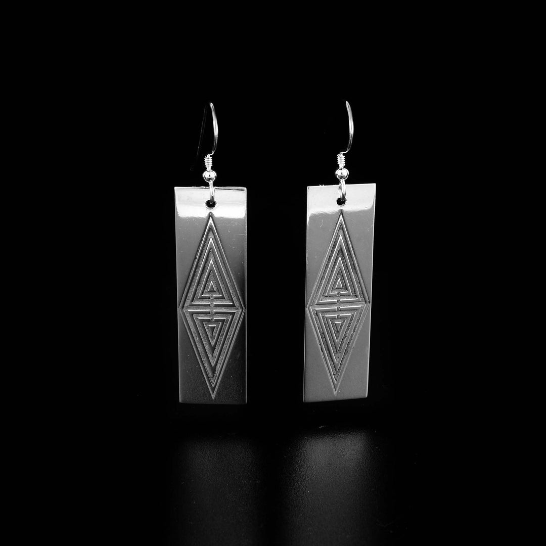 These rectangle dangle earrings are made from sterling silevr and have long, wide rectangular hangs. There triangle designs in the center of the hangs that resemble patterns from traditional Raven's tail weaving.