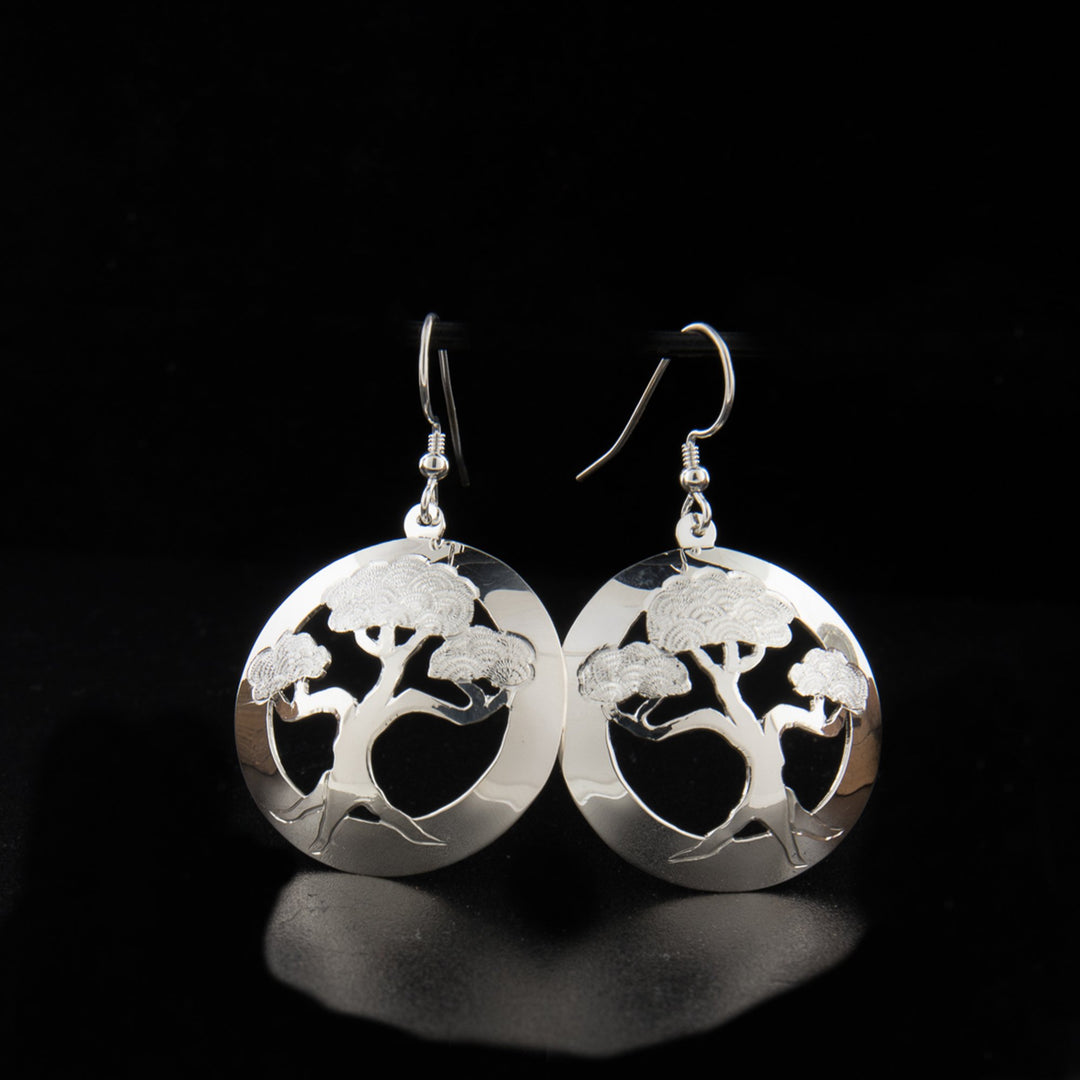 These dangling bonsai tree earrings have circle shaped hangs made from sterling silver. There are cutouts in the center around a bonsai tree and carvings made on it detailing he tree.