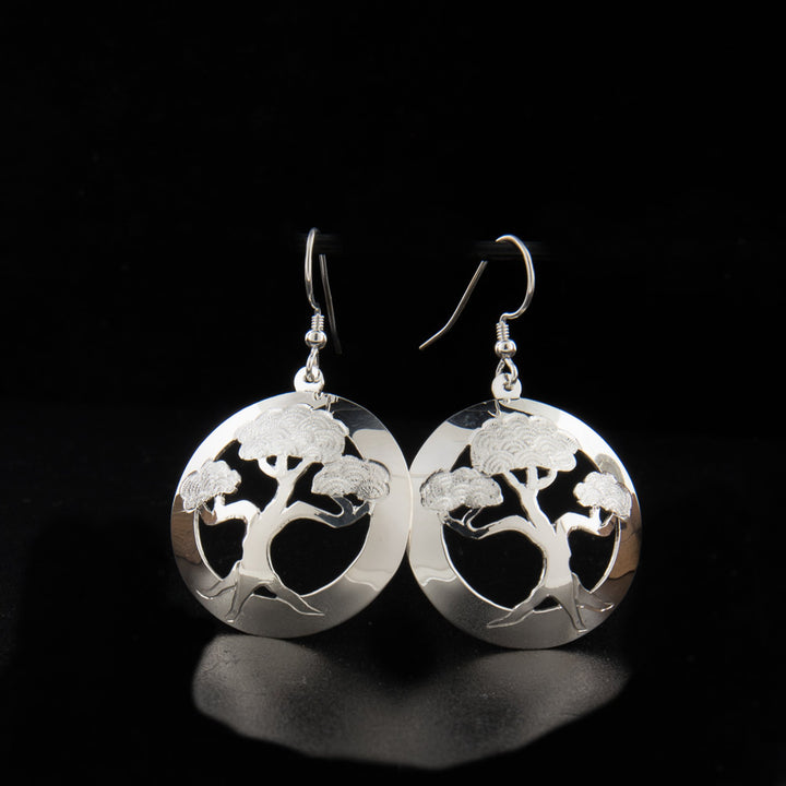 These dangling bonsai tree earrings have circle shaped hangs made from sterling silver. There are cutouts in the center around a bonsai tree and carvings made on it detailing he tree.