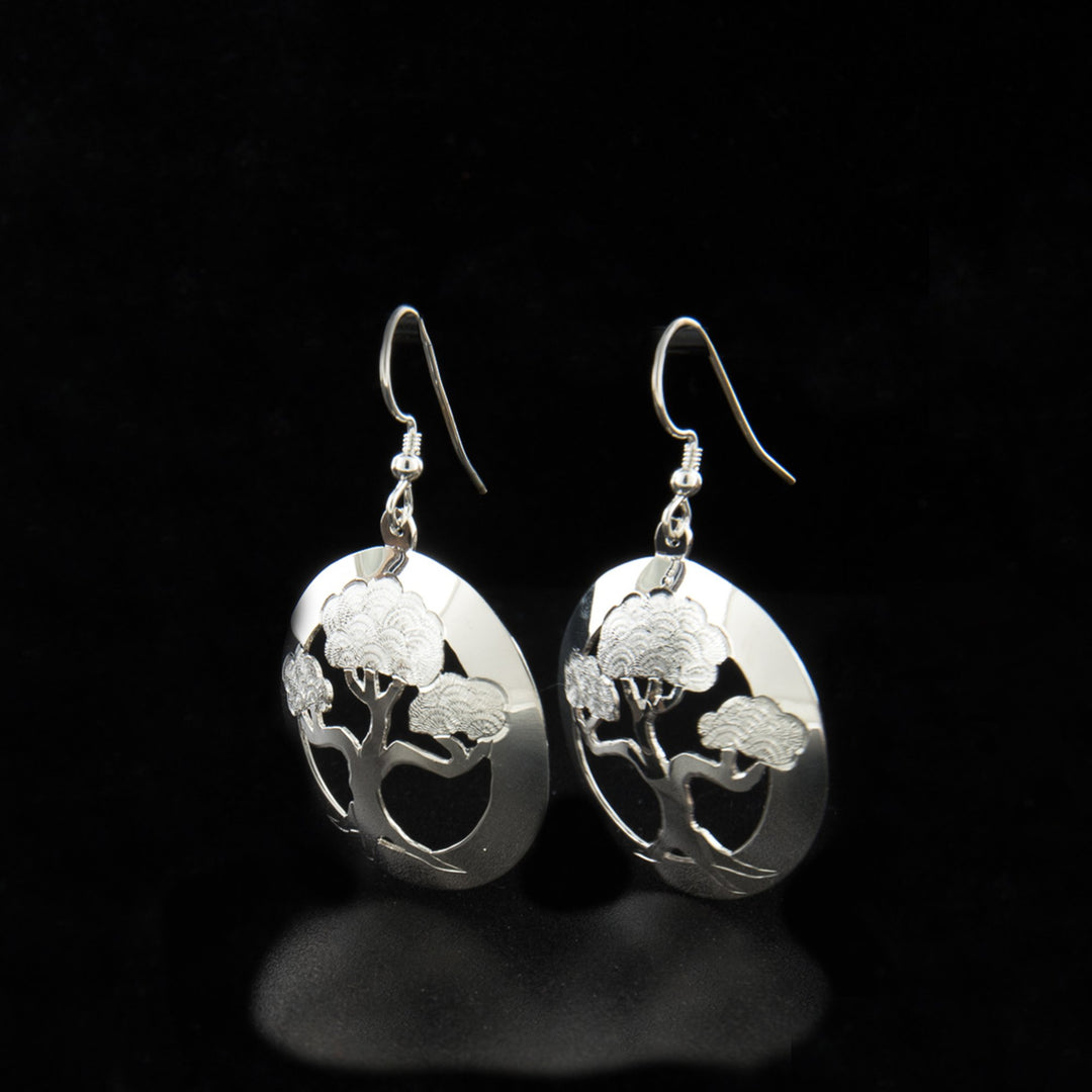 These dangling bonsai tree earrings have circle shaped hangs made from sterling silver. There are cutouts in the center around a bonsai tree and carvings made on it detailing he tree.