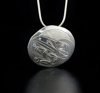 Round raven pendant hand-carved by Kwakwaka'wakw artist Don Lancaster. Made of sterling silver. Pendant is 1.25" in diameter. Hidden bail on back. Chain not included.