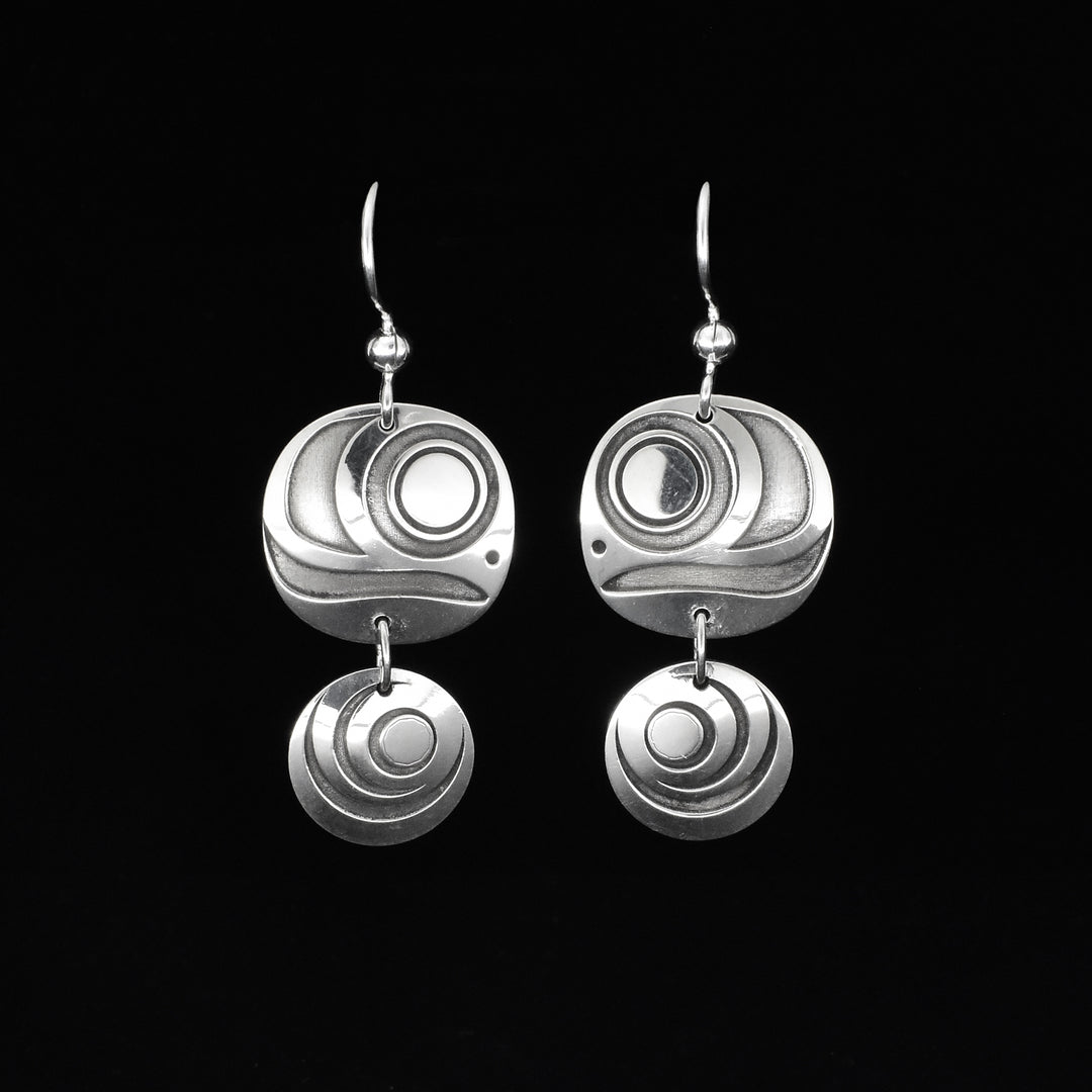 These elegant circle drop earrings are made from sterling silver and depict eggs of the Salmon. The pieces have dangling, circle shaped hangs with smaller circle hangs below them. There are designs cast into the surface of the hangs that look like Salmon eggs