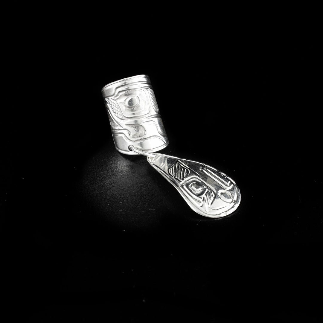 Ear cuff hand-carved by Heiltsuk artist Ivan Wilson. Made of sterling silver. There is an eagle carved into the cuff and another carved into the dangling teardrop adornment. Ear cuff is 1.88" long including teardrop eagle and cuff is 0.50" wide.