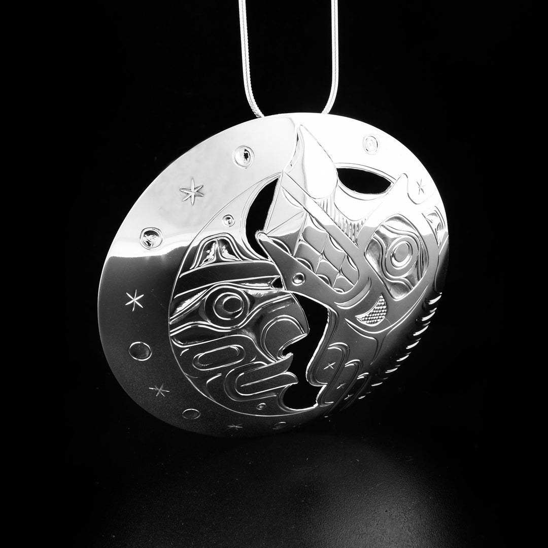 This Wolf and Moon pendant is made from sterling silver and has a large circle shape with cutout details on it. There are carvings on the surface of the pendant depicting the Wolf and the Moon.