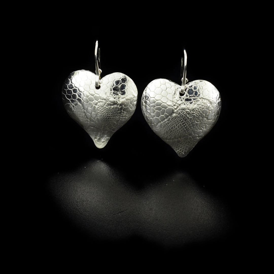 These sterling silver heart earrings have heart shaped hangs that dangle from the hooks. There is a textured design featured on the hangs that has been achieved by embossing the surface of them using French lace.