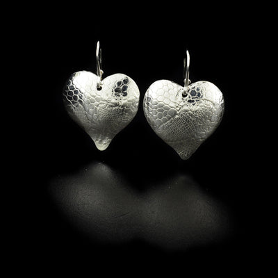 Sterling Silver Venice Hearts Earrings by Victoria Poyton. Each earring is in the shape of a heart. The ear hook is attached at the very top of each heart. The artist has used French lace to emboss the design on each heart.