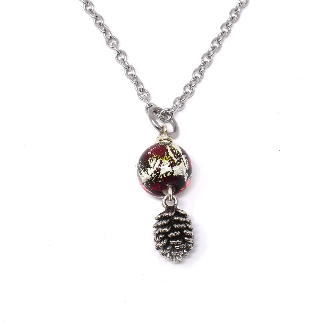 This pinecone necklace is made from a red lampworked bead with gold leaf, a stainless steel chain and a detailed, silver plated pinecone charm. The stainless steel chain has a red, glass bead with gold leaf in it and a silver filled pinecone charm below the bead.