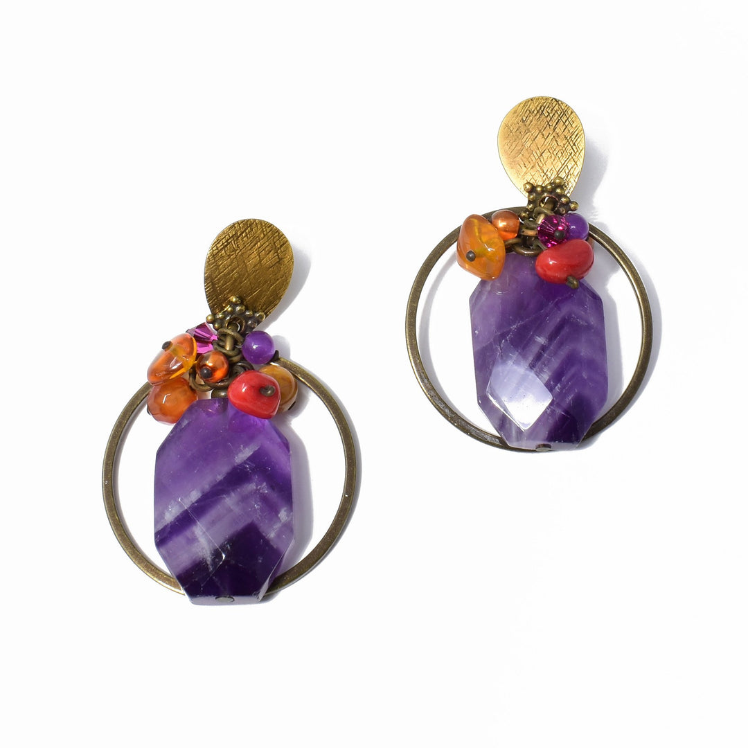 These chunky amethyst stud earrings are made from amber, genuine amethyst, glass, mother of pearl, carnelian agate, and Austrian crystal. There is a cluster of amber, glass and crystal beads at the top of the brass hooks. There are large, rectangular amethyst gems in the center of the piece and and a large, brass hoop going around the whole piece.