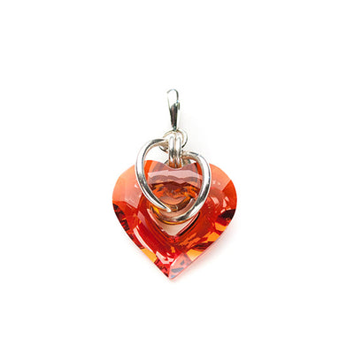 U Captured My Heart Persimmon Pendant by Lisa Rideout. The Swarovski crystal pendant is in the shape of a heart. The artist has included sterling silver accents in the form of loops that go through the center of the heart pendant.