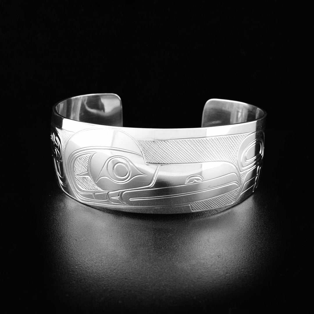 This sterling silver cuff bracelet has a single wide band with a gap in the back. There is a depiction of the Raven carved into the surface of the band.