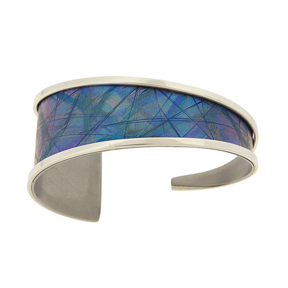 This titanium bracelet cuff is made from sterling silver and anodized titanium. It has a single band that tapers from 1" to 1/8" with a gap in the back. The band is made form titanium and is blue with designs achieved by anodizing the metal. There are silver accents surround the band.